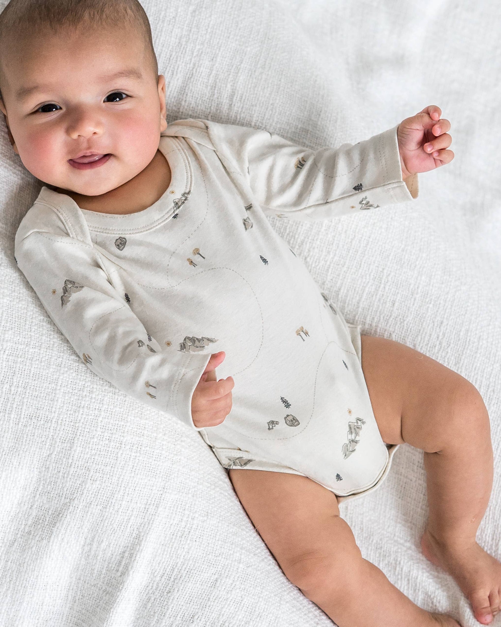Baby wearing a white long-sleeve onesie with small patterns on a white blanket
