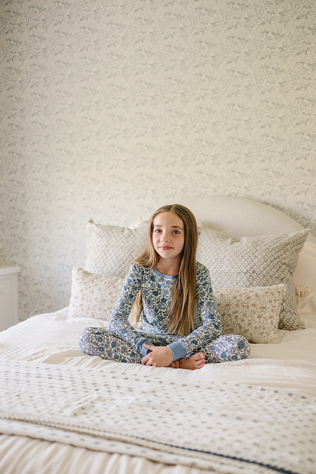 Young girl sitting on a bed with patterned wallpaper in the background