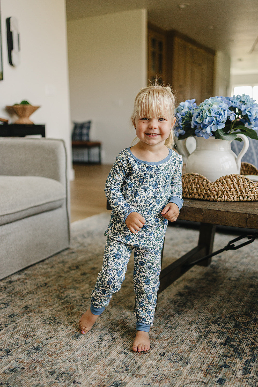 Child wearing blue floral pajamas standing in a living room.