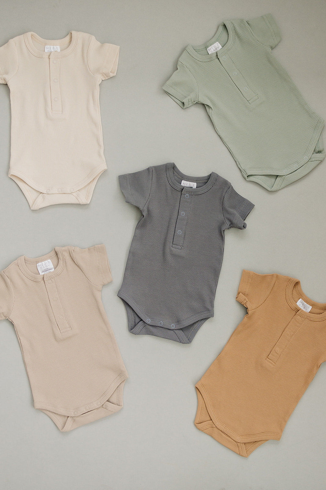 Five baby rompers in beige, gray, and brown on a neutral background