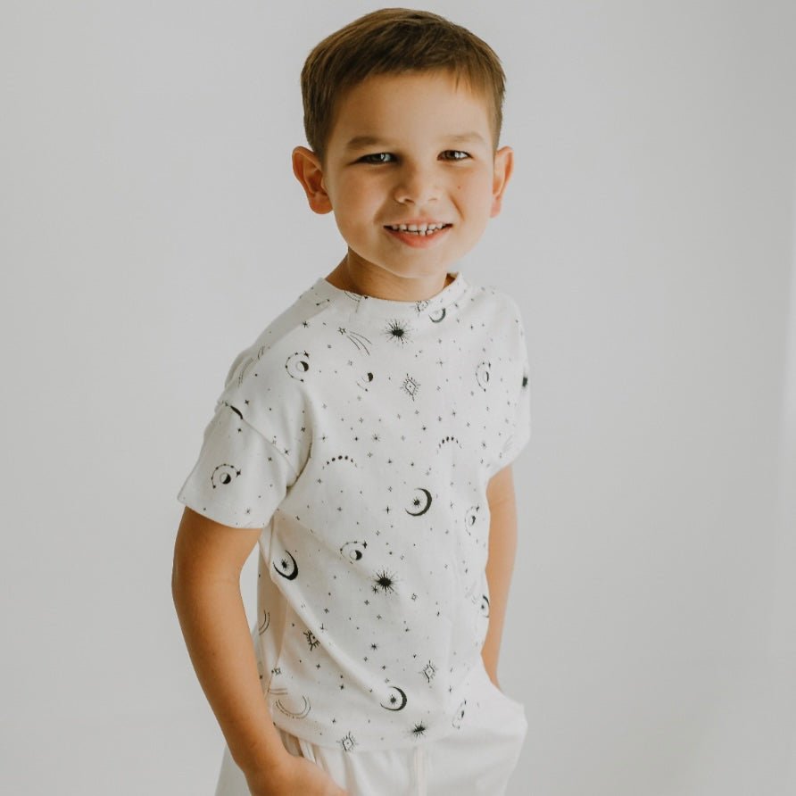 Child wearing a white t-shirt with black patterns on a plain background