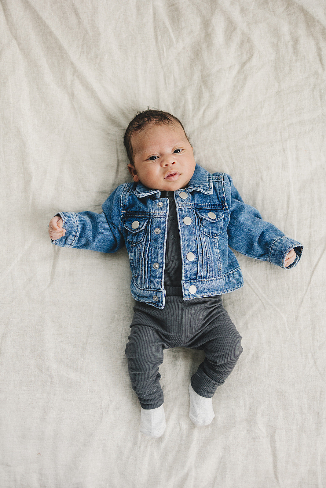 Baby wearing a denim jacket lying on a light-colored blanket
