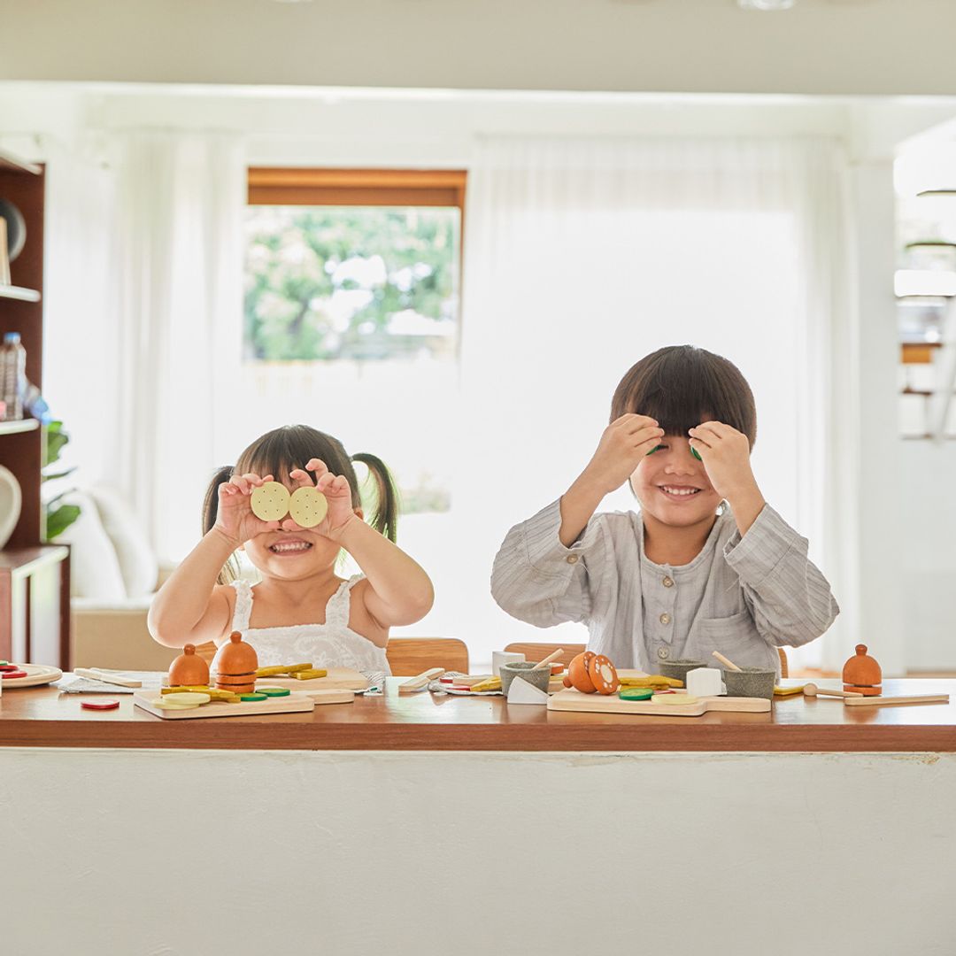 Two children playing with toy vegetables at a table in a bright room.