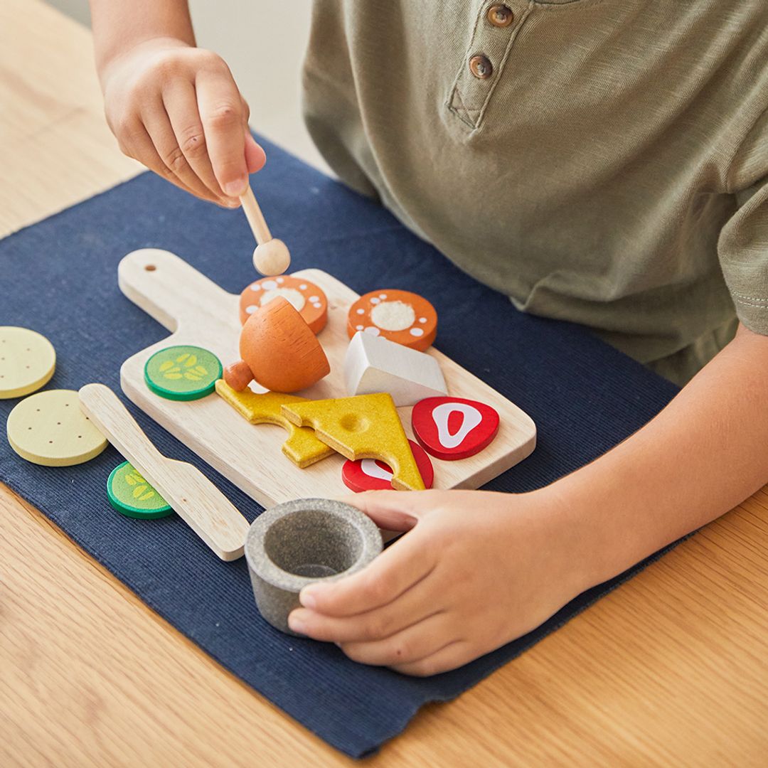 Child playing with a wooden toy kitchen set on a blue placemat.