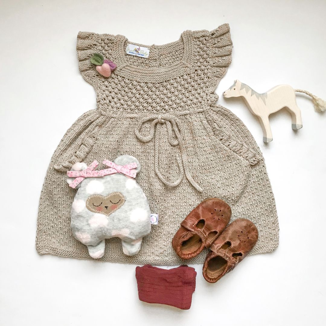 Knitted baby dress with toys and shoes on a white background