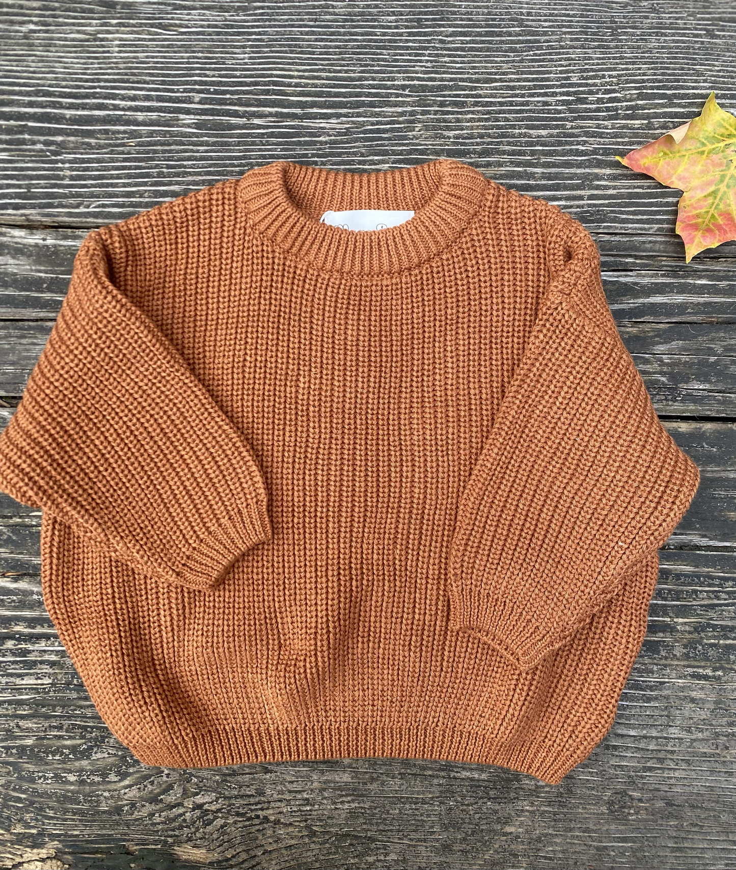 Clay knitted sweater on a wooden surface with a leaf