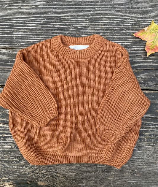 Clay knitted sweater on a wooden surface with a leaf