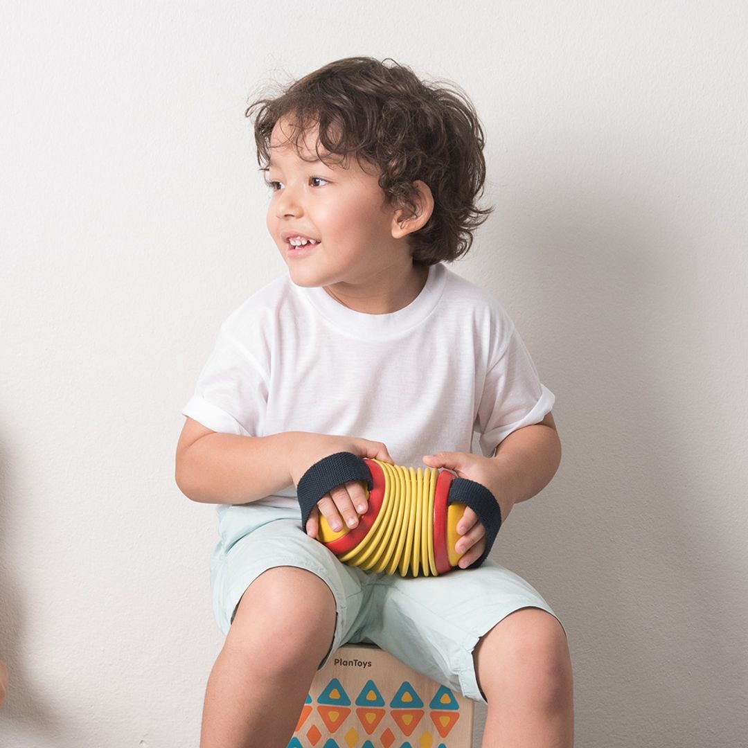 Child holding a colorful ball on a patterned stool against a plain background