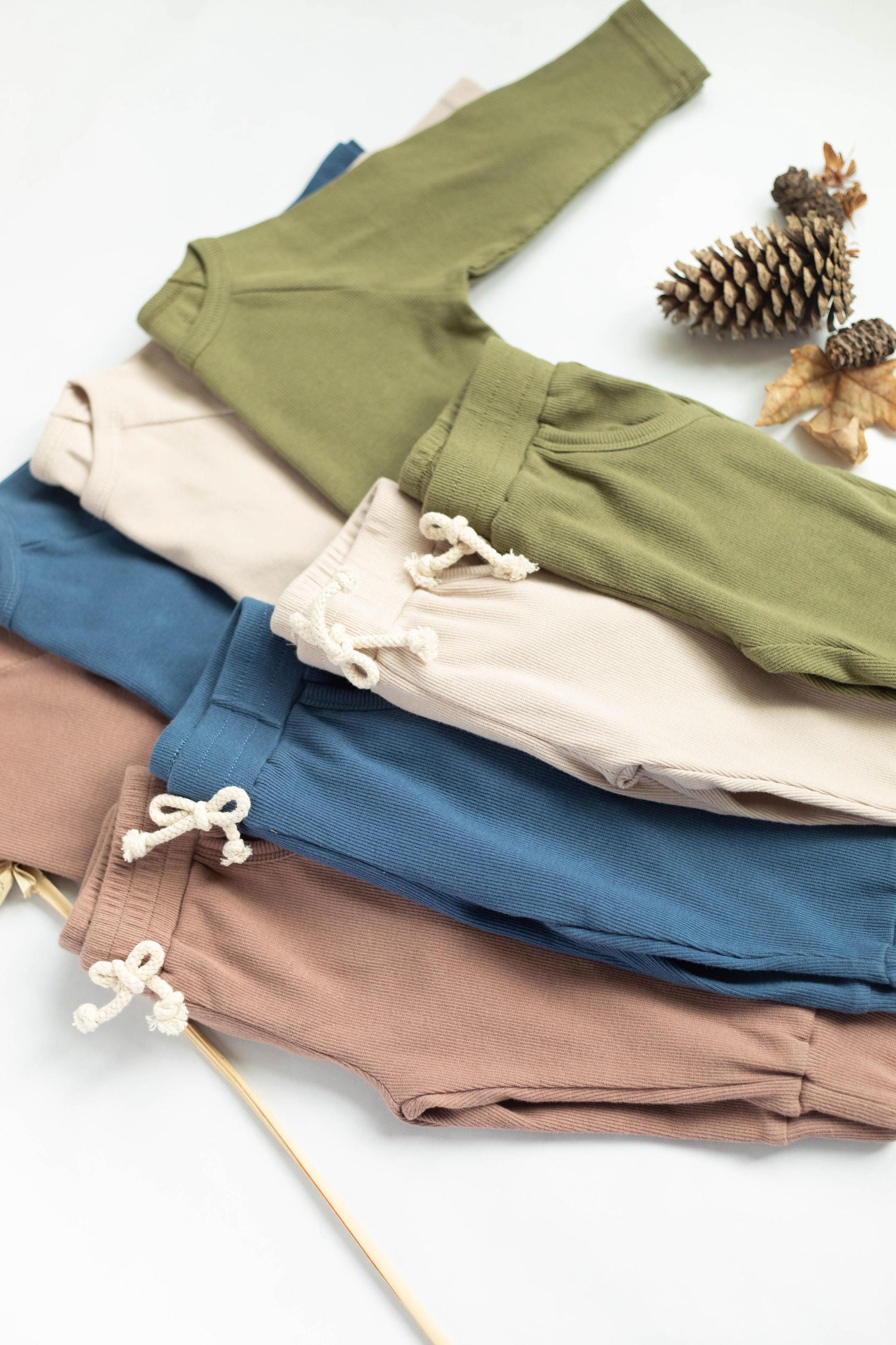 Stack of folded pants in green, blue, beige, and brown on a white background.