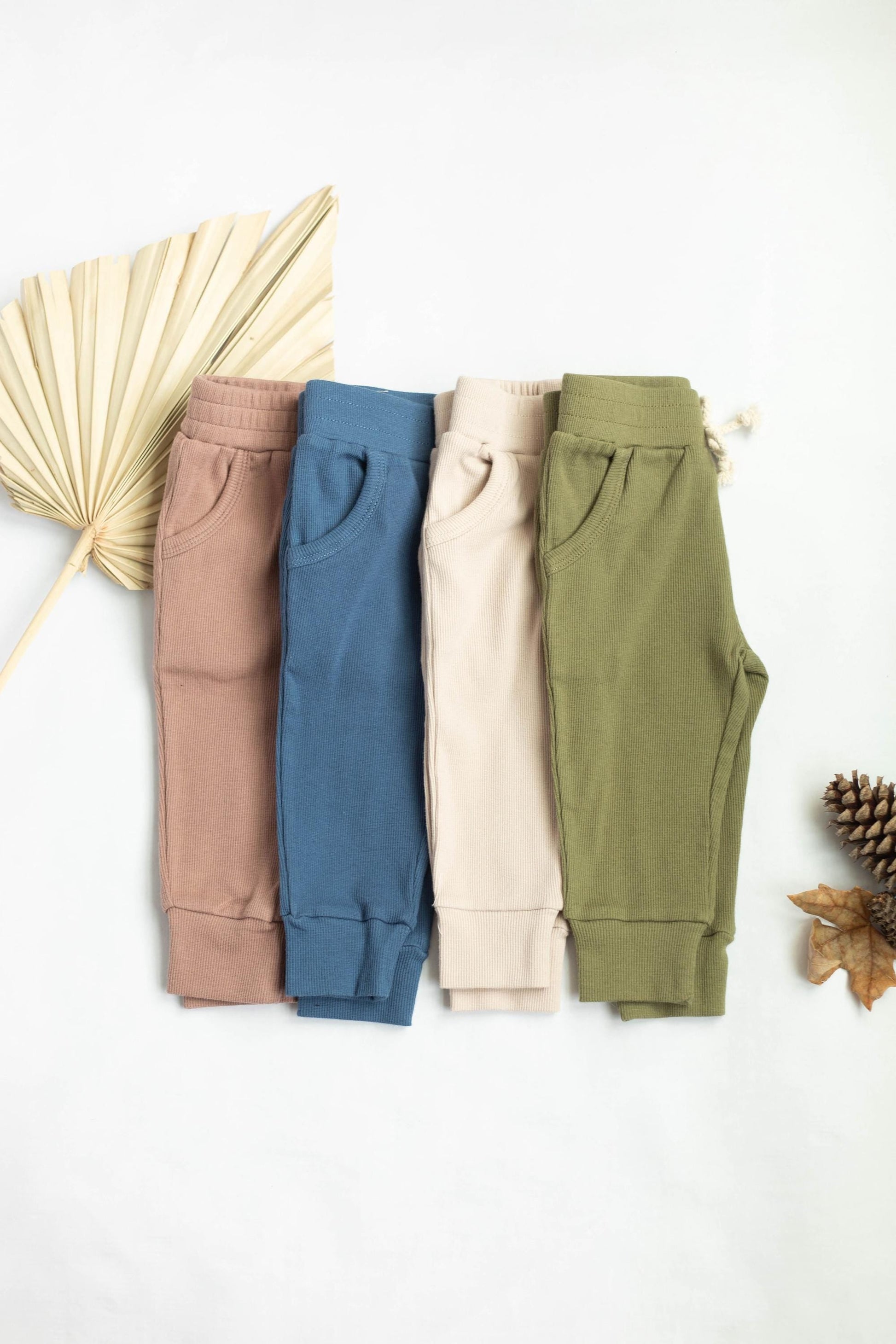 Four pairs of jogger pants in different colors on a white background with decorative elements.
