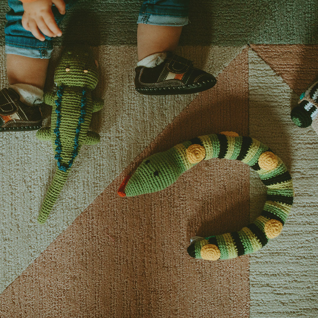Knitted toy snake on a textured carpet with a child's feet in the background.