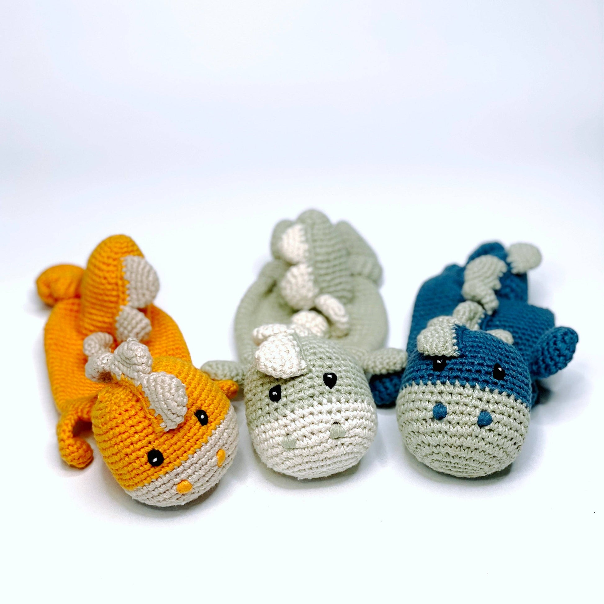 Three crocheted dinosaur toys in orange, gray, and blue on a white background