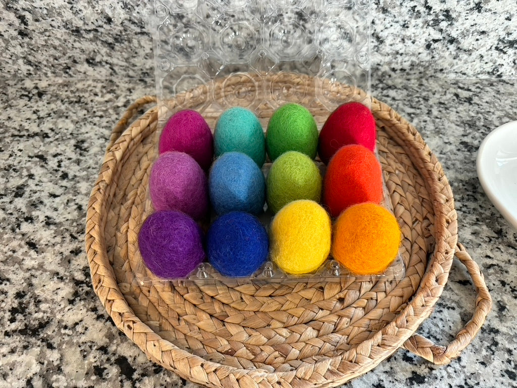 Set of colorful felt balls in a clear plastic bag on a woven mat.