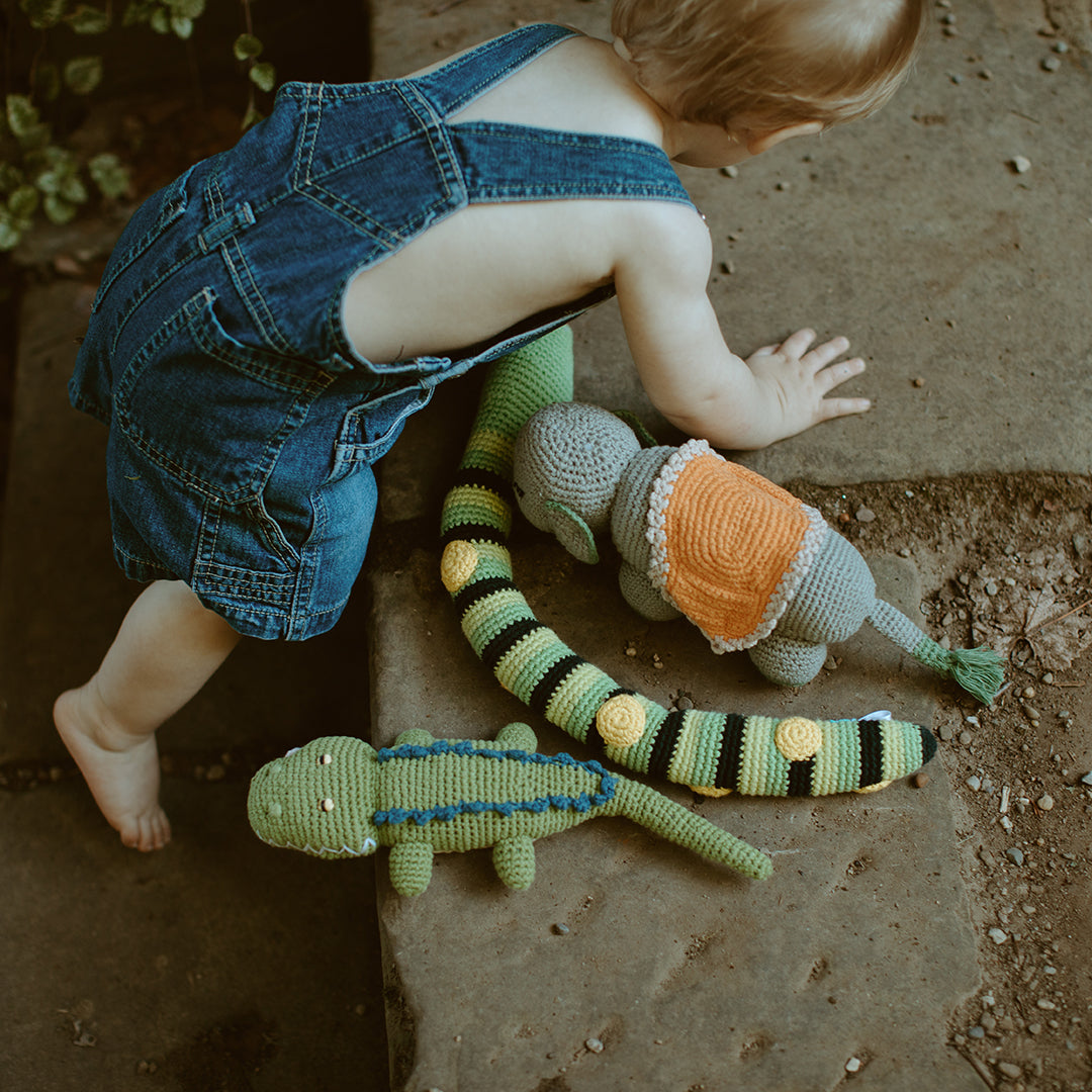 Child playing with crocodile and elephant plush toys on a concrete floor.