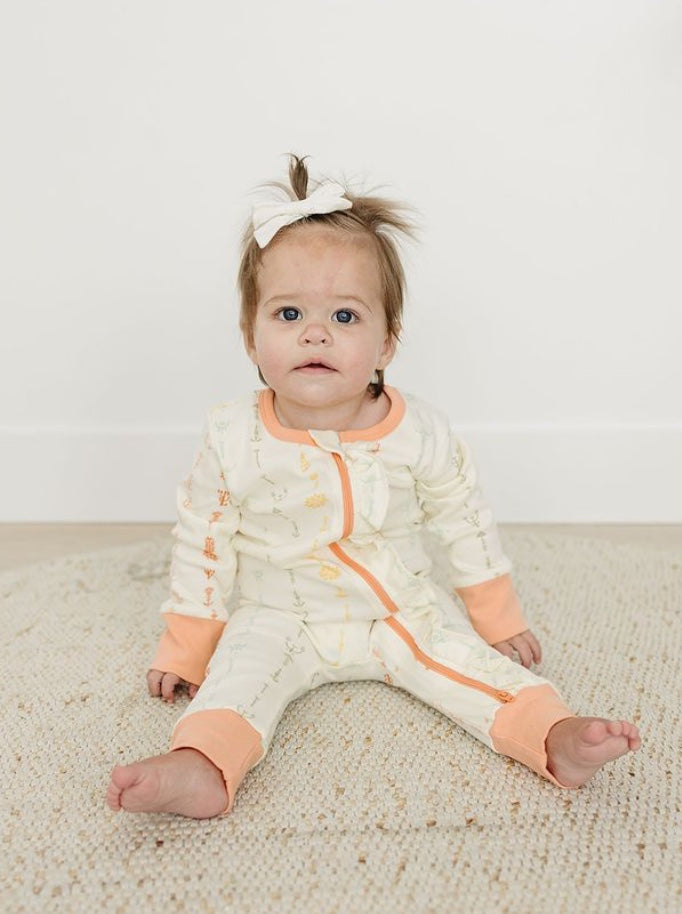Baby wearing a white and orange outfit sitting on a beige carpet.