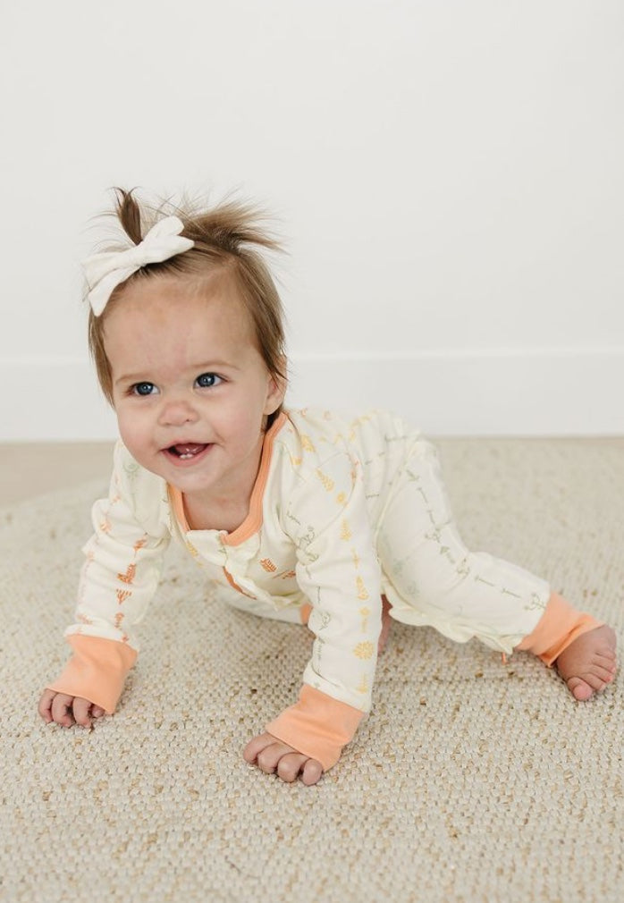 Baby in a white and orange outfit with a bow on a beige carpet