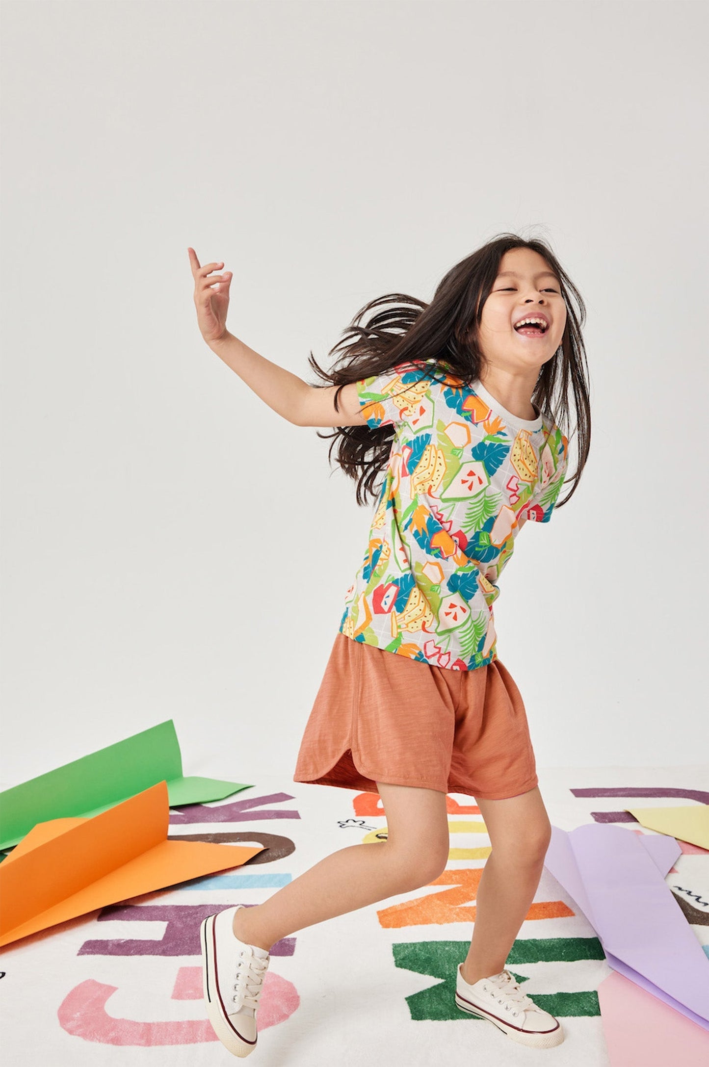 Child wearing a colorful floral shirt and orange skirt on a white background