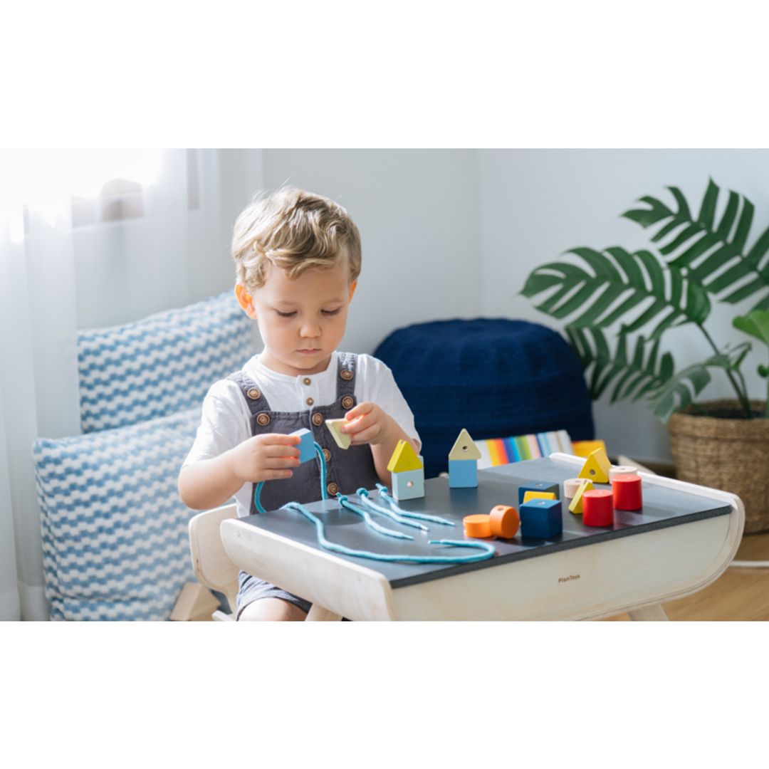 Child playing with toys on a high chair in a bright room with plants