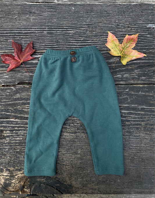 Green ribbed knit pants on a wooden surface with autumn leaves.