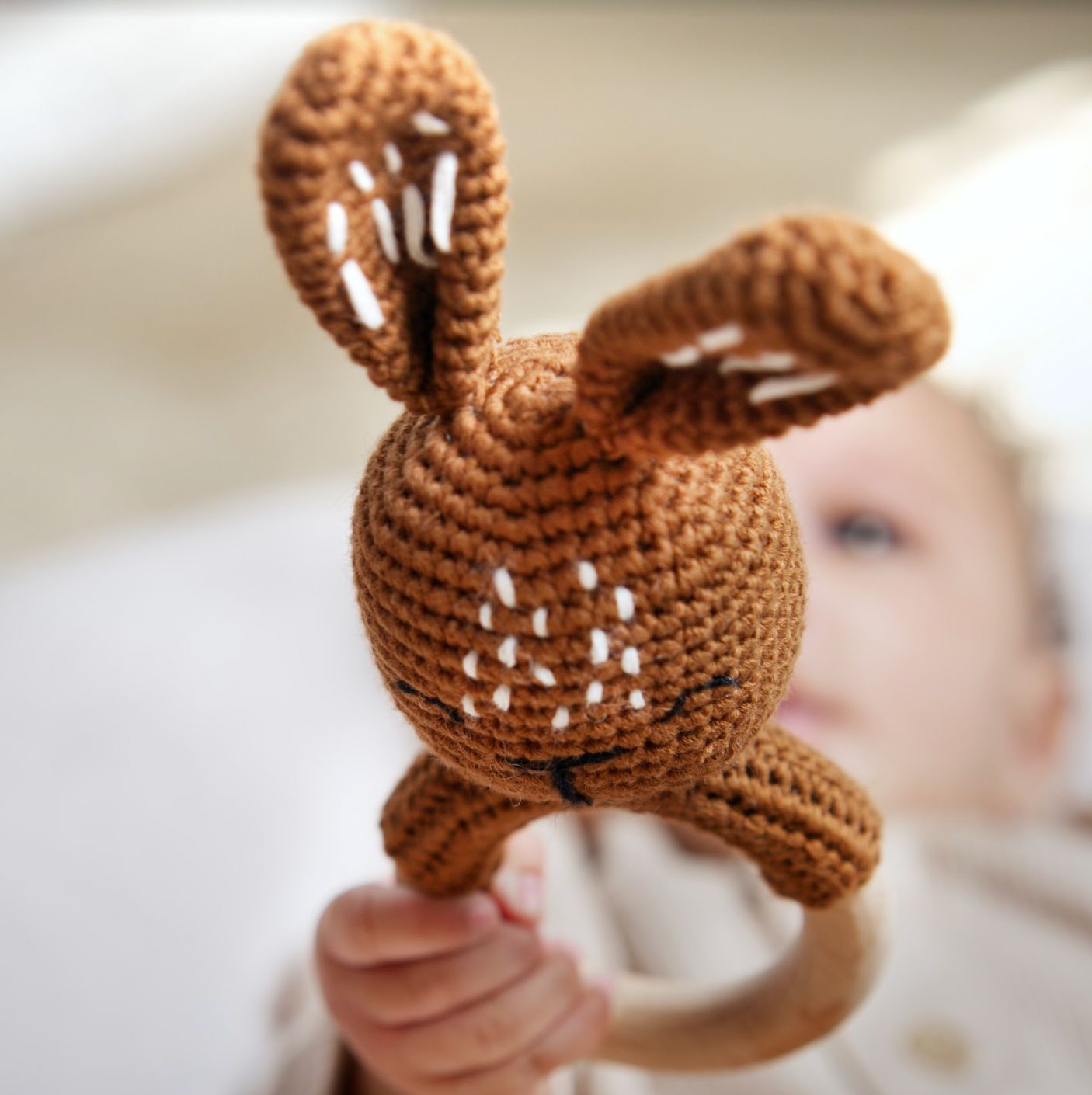 Brown crochet deer toy held by a child with a blurred background