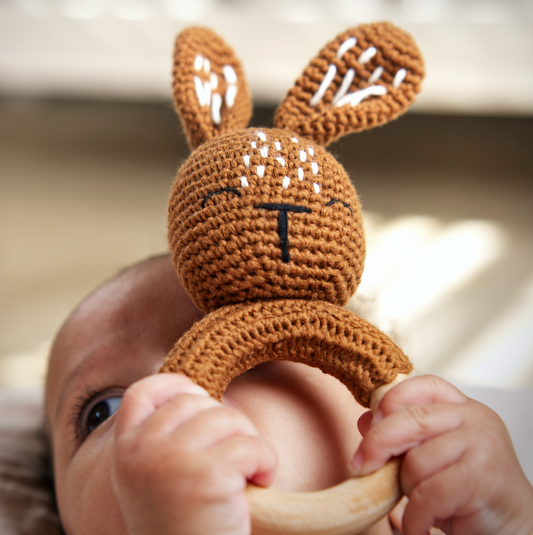 Baby holding a brown knitted bunny rattle toy