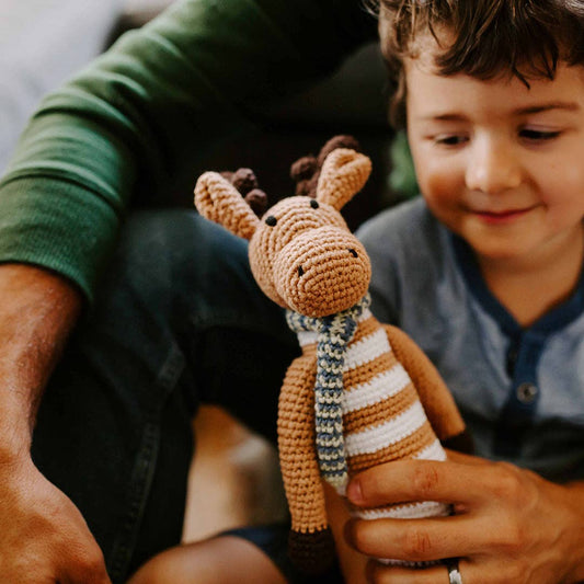 Child holding a crocheted moose toy with a striped scarf, sitting next to an adult.