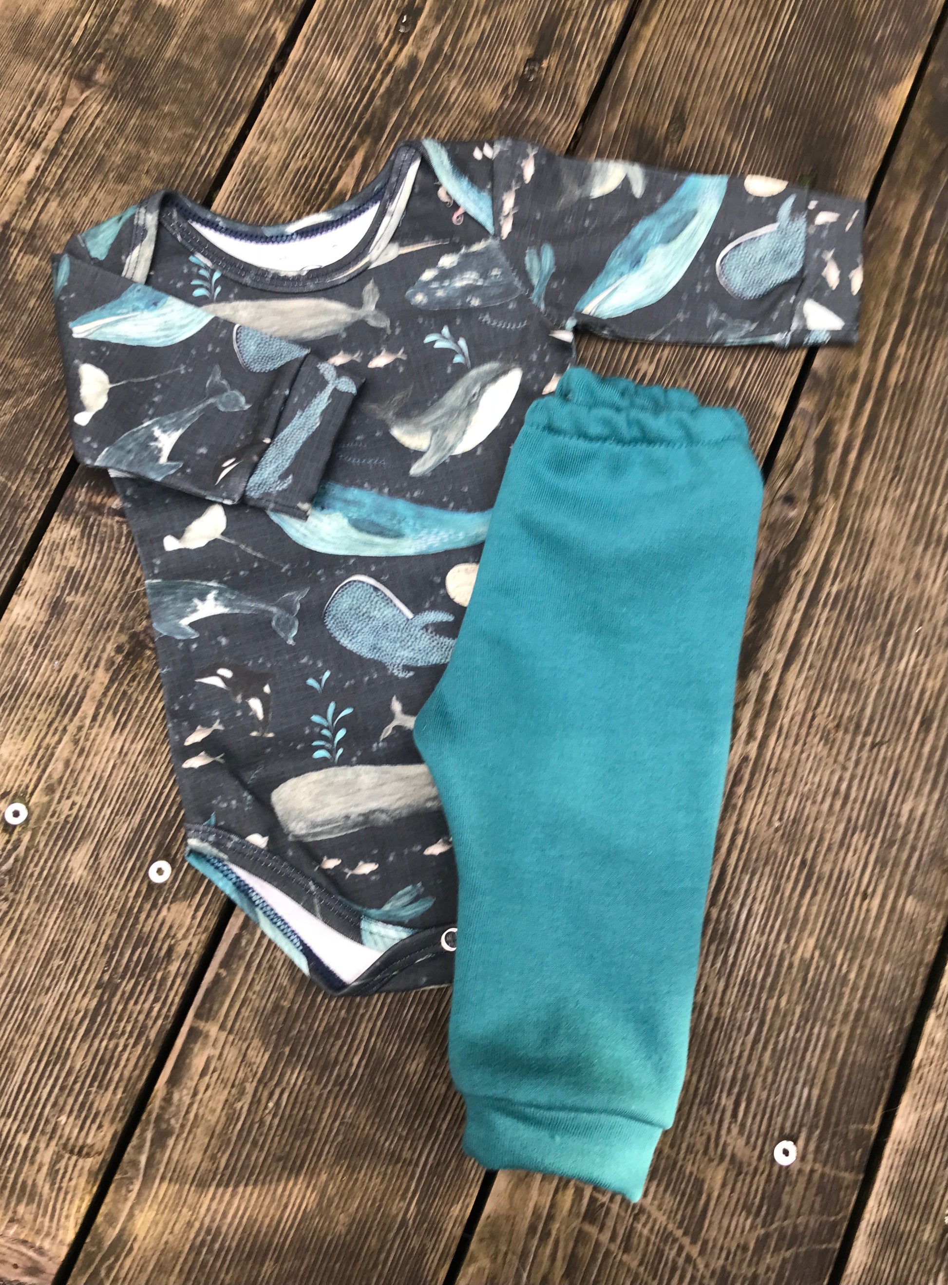 Baby outfit with whale pattern top and teal pants on a wooden surface