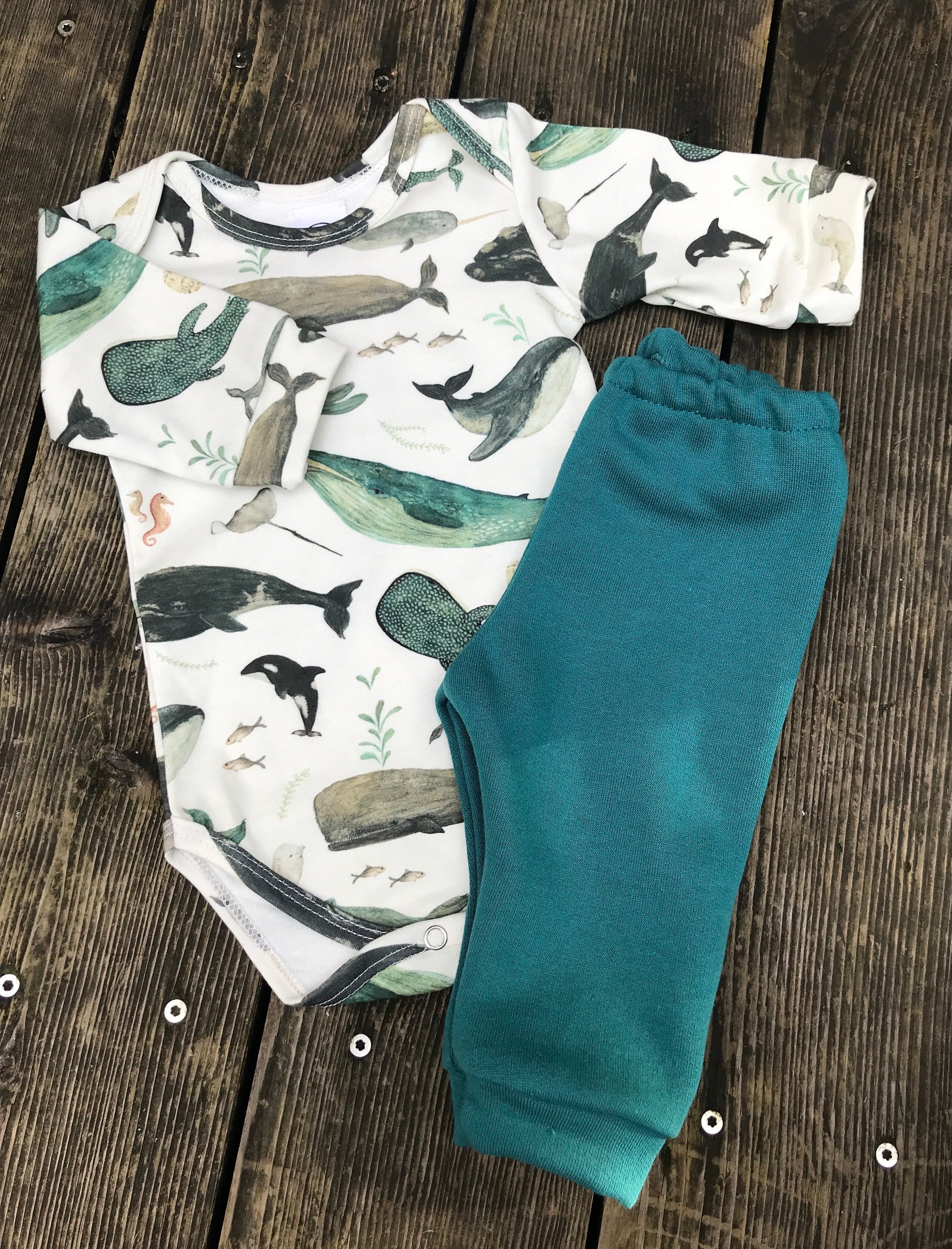 Baby onesie with whale pattern and teal pants on a wooden surface