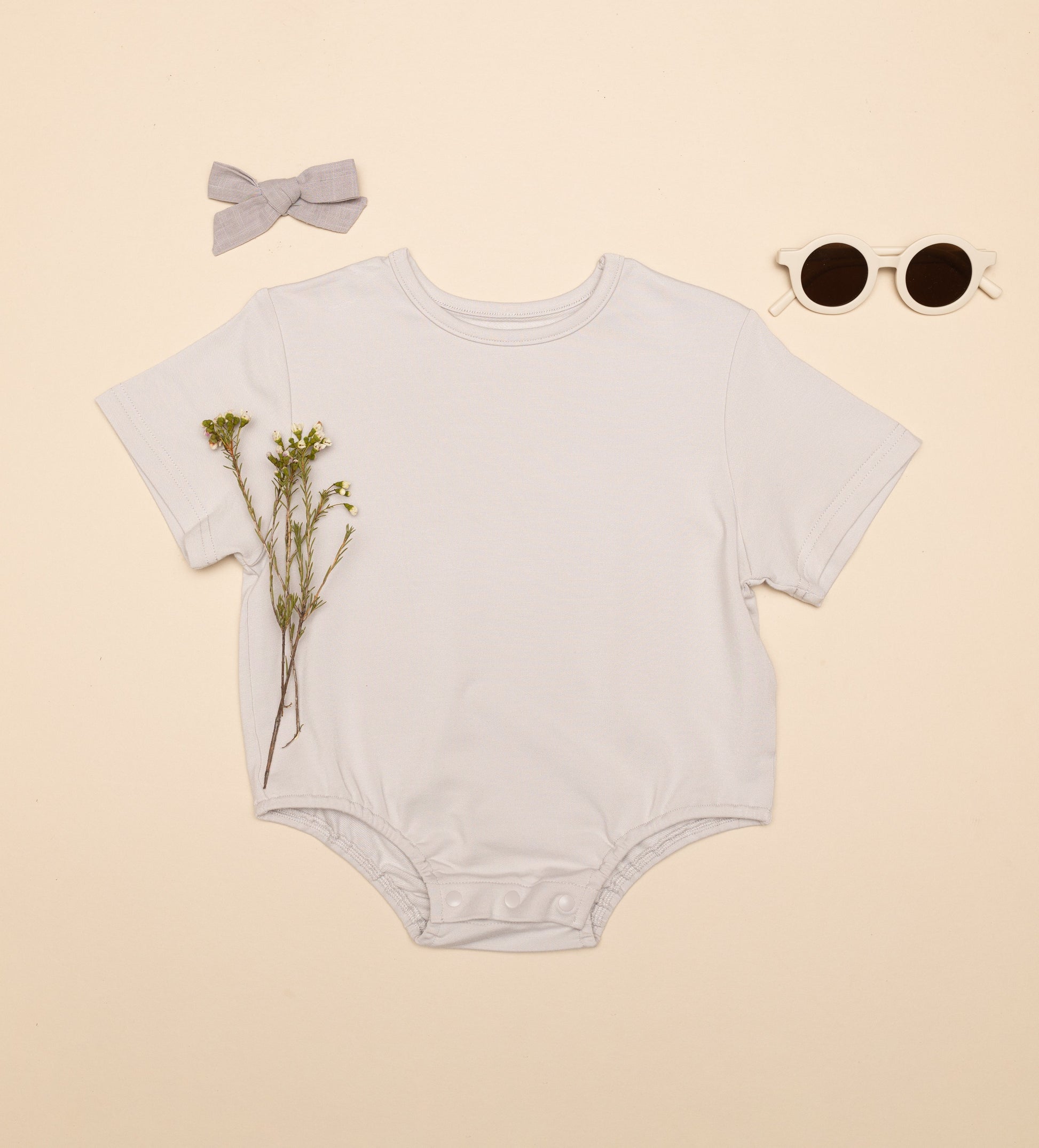 Baby onesie with a bow, sunglasses, and flowers on a beige background