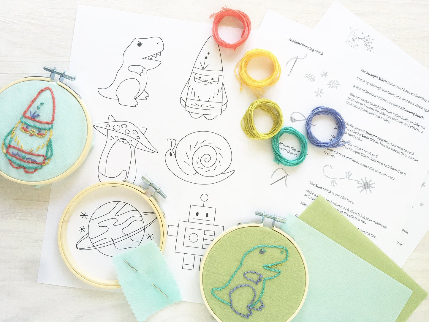 Embroidery hoops with pre-designed patterns on a table with embroidery threads and instructions.