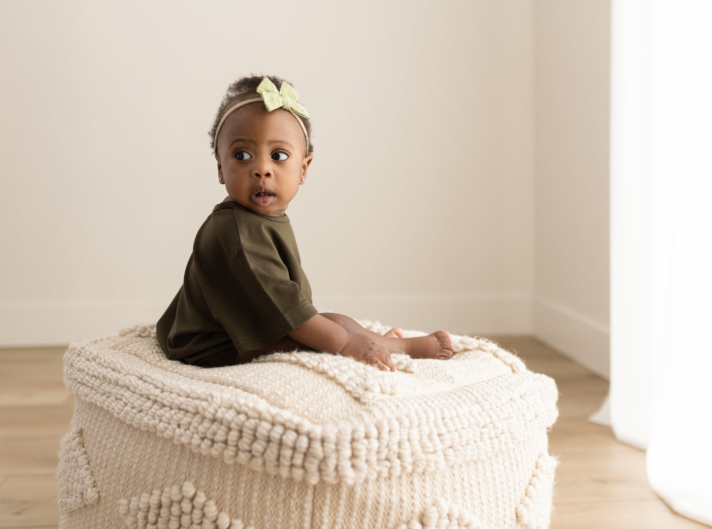 Baby sitting on a textured ottoman with a neutral background