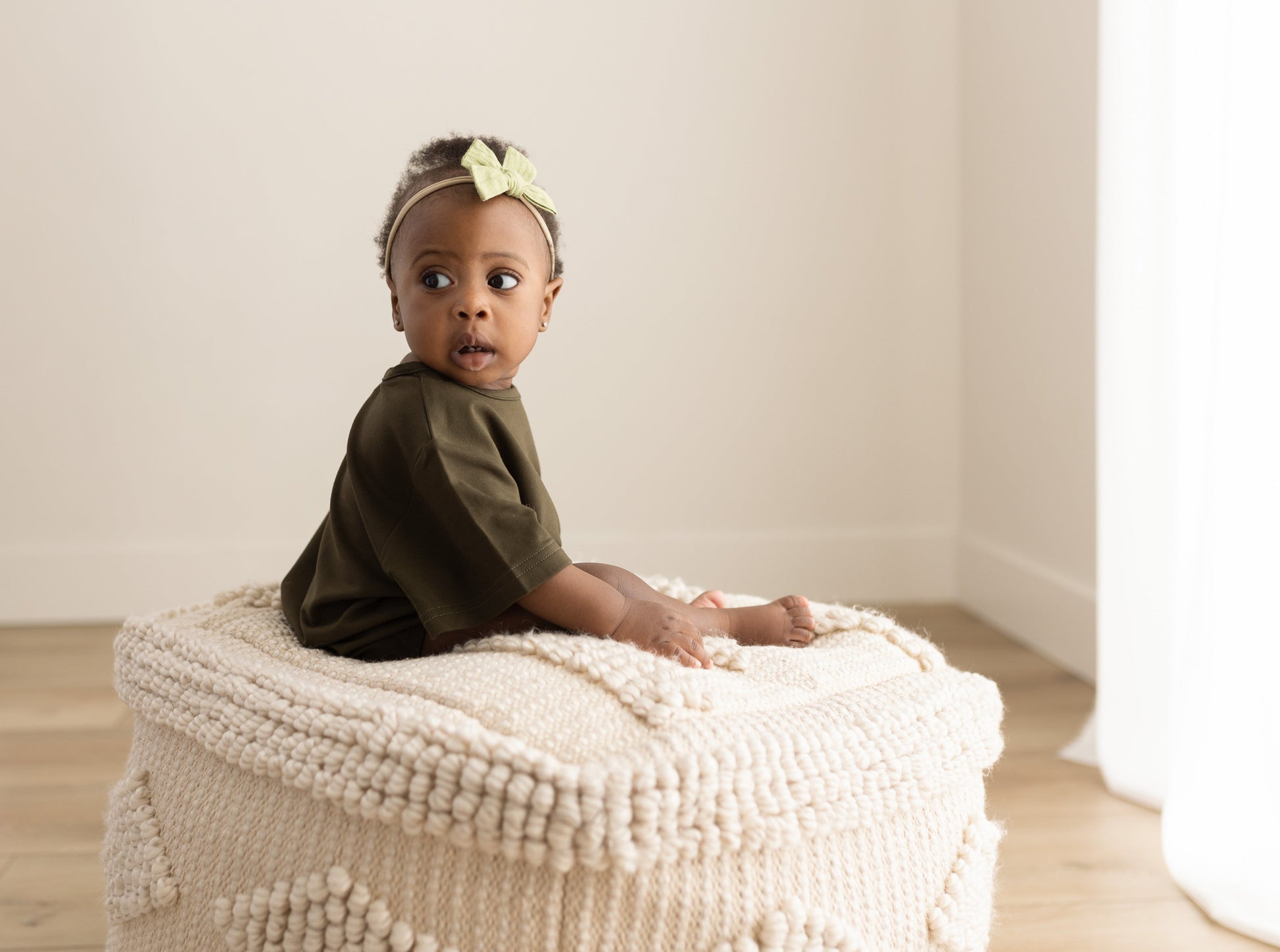 Baby sitting on a textured ottoman with a neutral background
