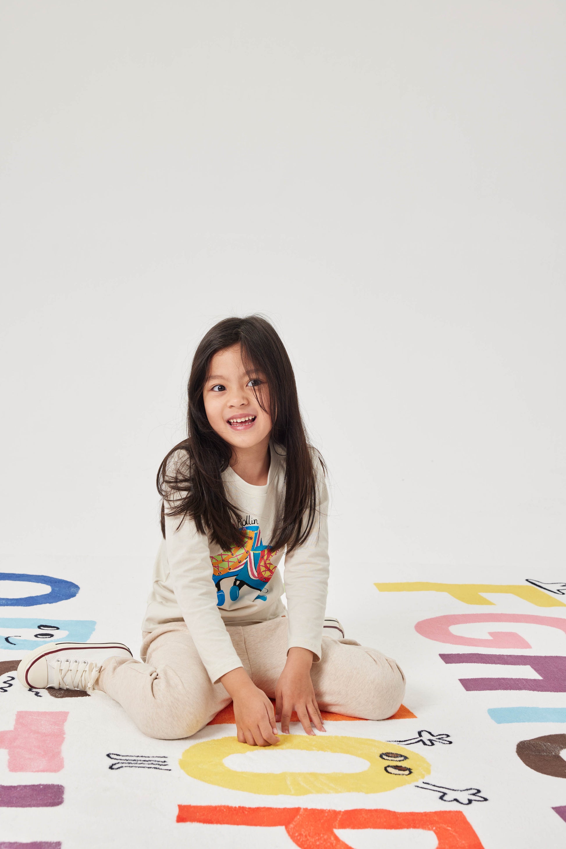 Child sitting on a colorful alphabet mat with a plain white background