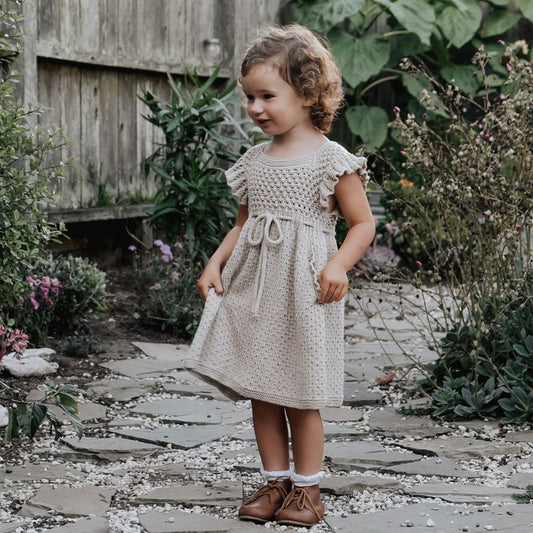 Young girl in a beige dress standing on a stone path in a garden.