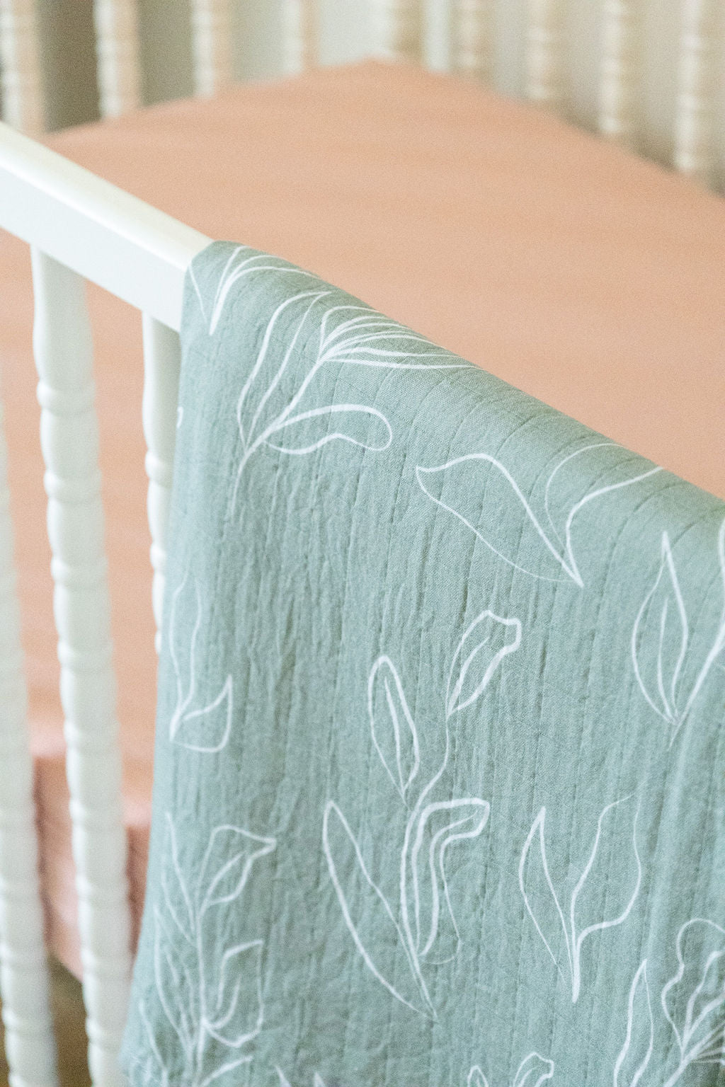 Light blue textured blanket with white leaf patterns draped over a crib.