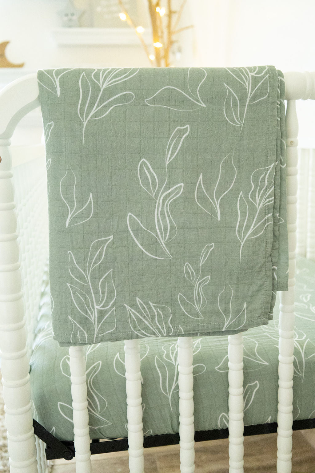 Green baby blanket with leaf pattern draped over a white crib
