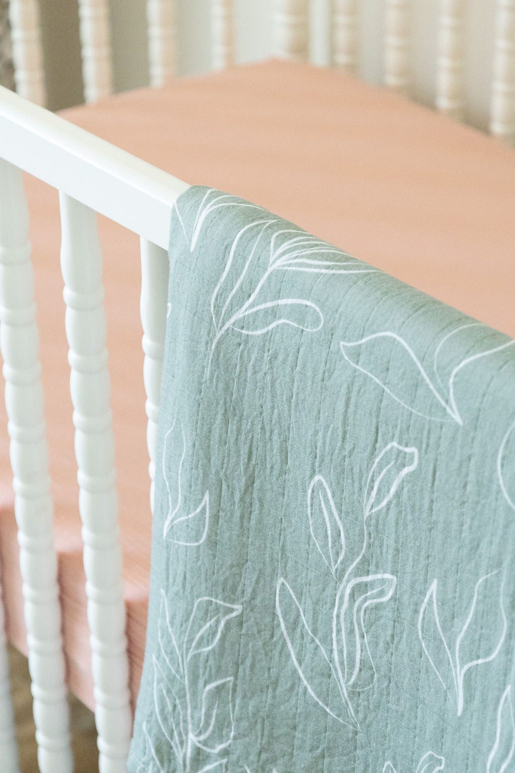 Teal crib sheet with white leaf pattern draped over a crib