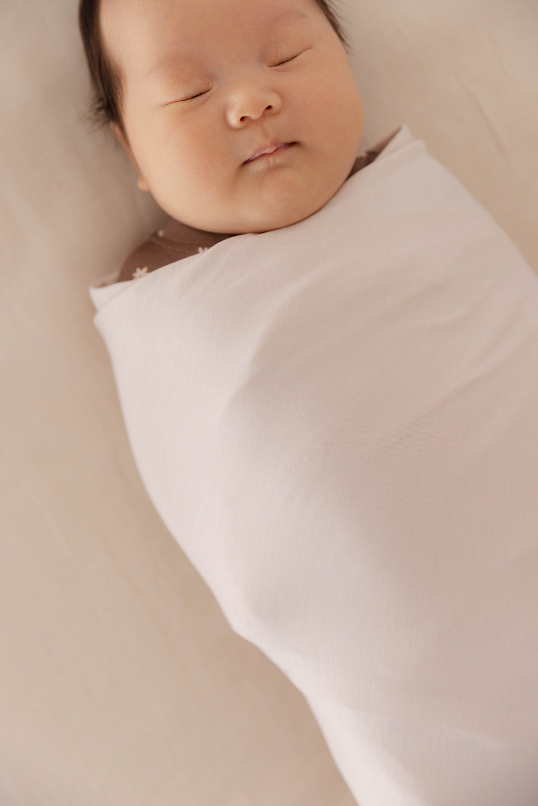 Newborn baby wrapped in a white blanket on a beige surface