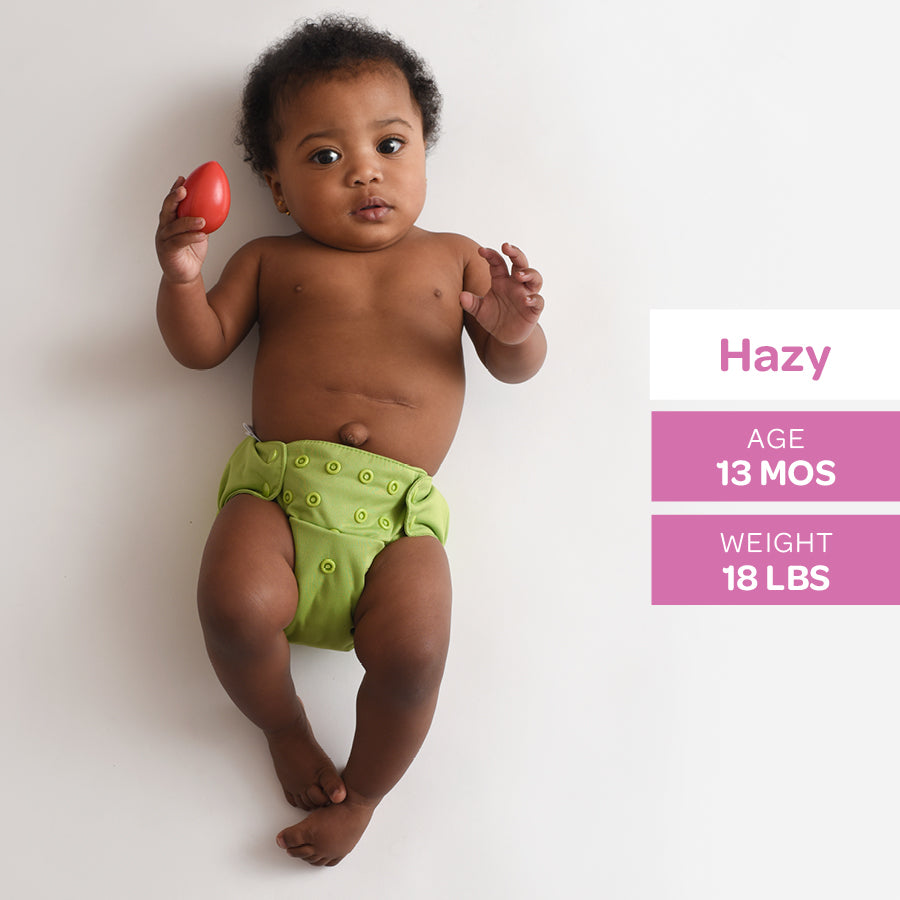 Baby wearing a green diaper holding a red object on a white background