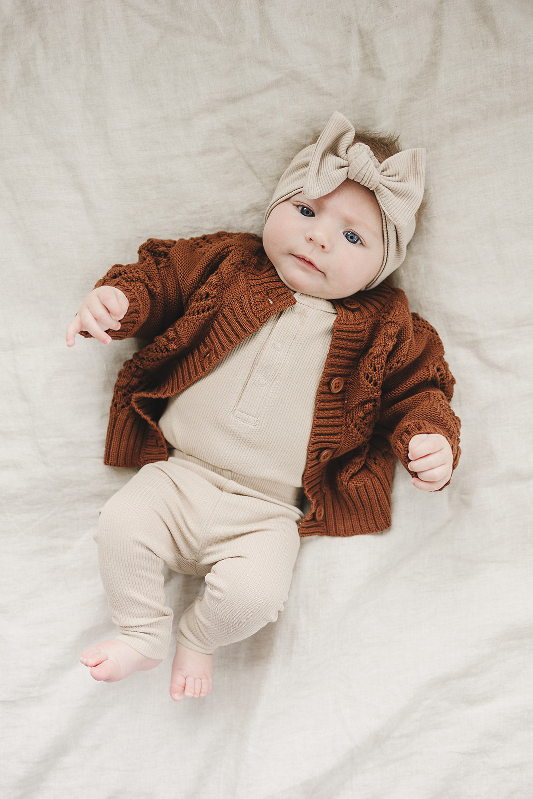 Baby wearing a brown cardigan and beige outfit with a matching headband on a light background