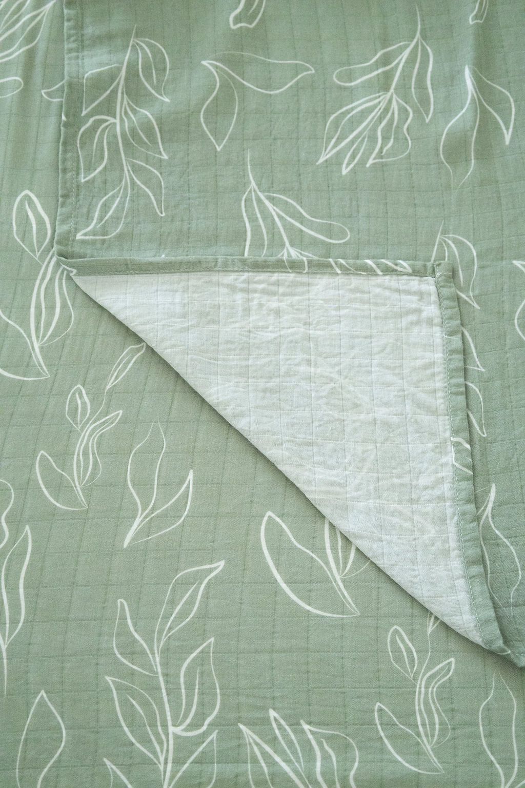 Green fabric with white leaf patterns and a folded section showing texture.