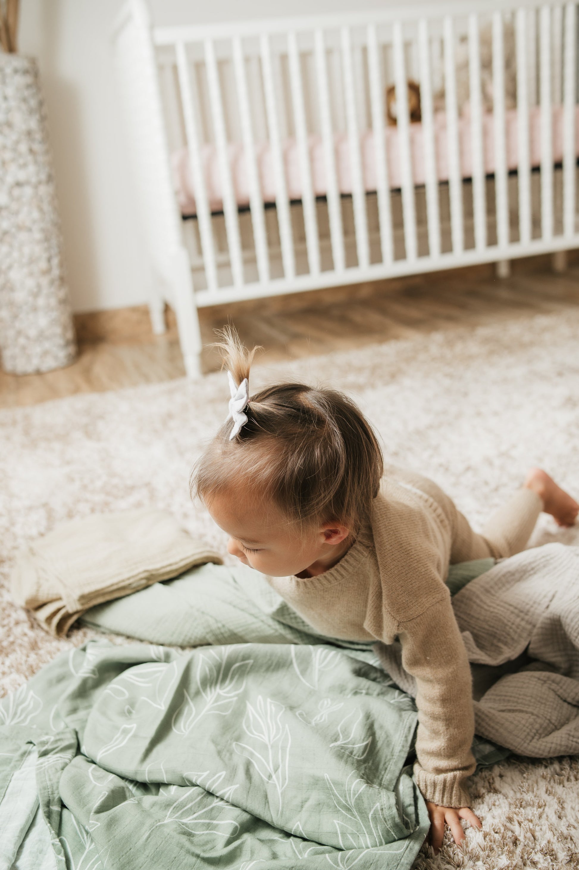 Baby lying on a green blanket in a nursery with a white crib in the background.