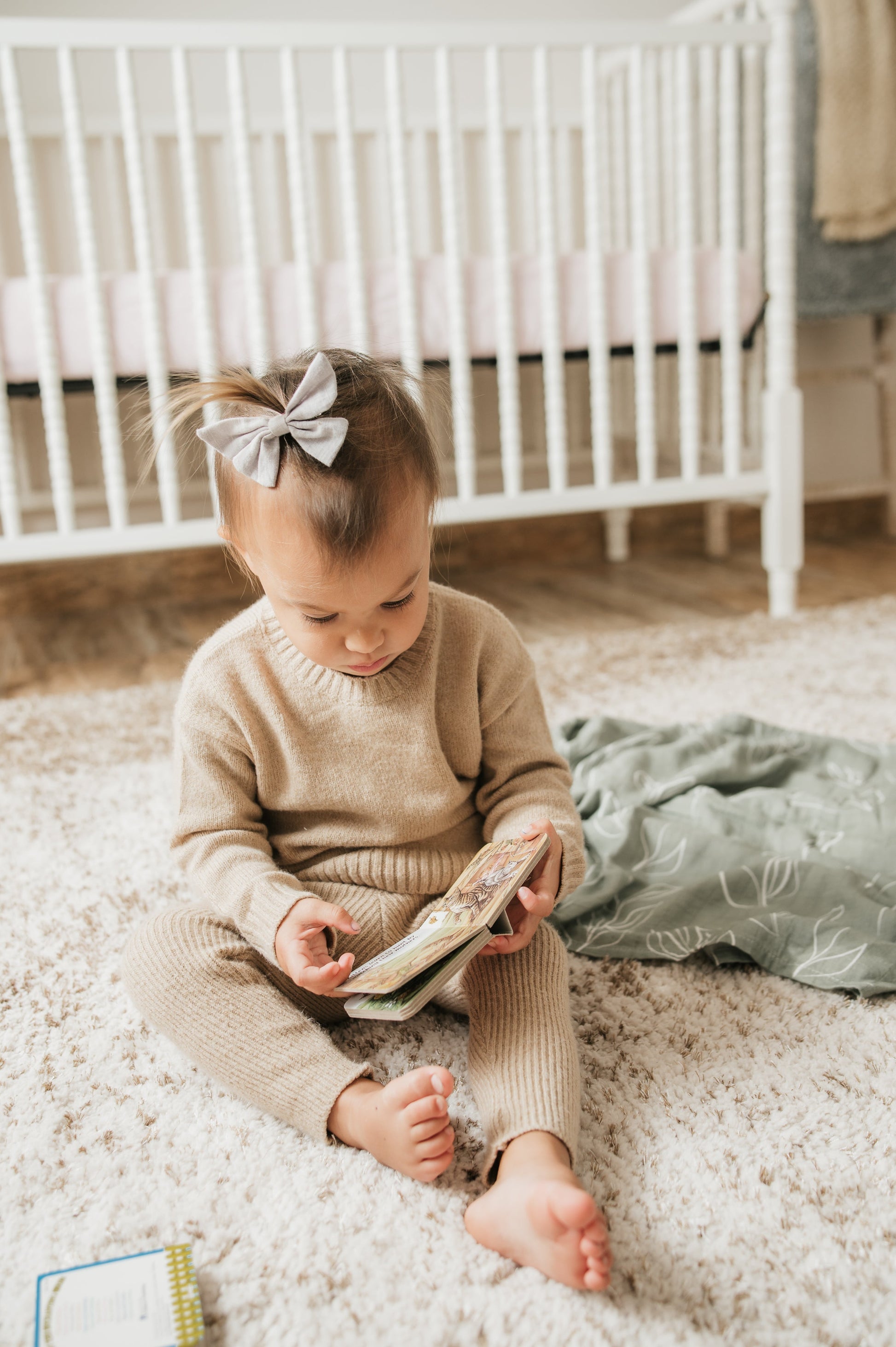 Child sitting on a carpeted floor reading a book in a nursery.