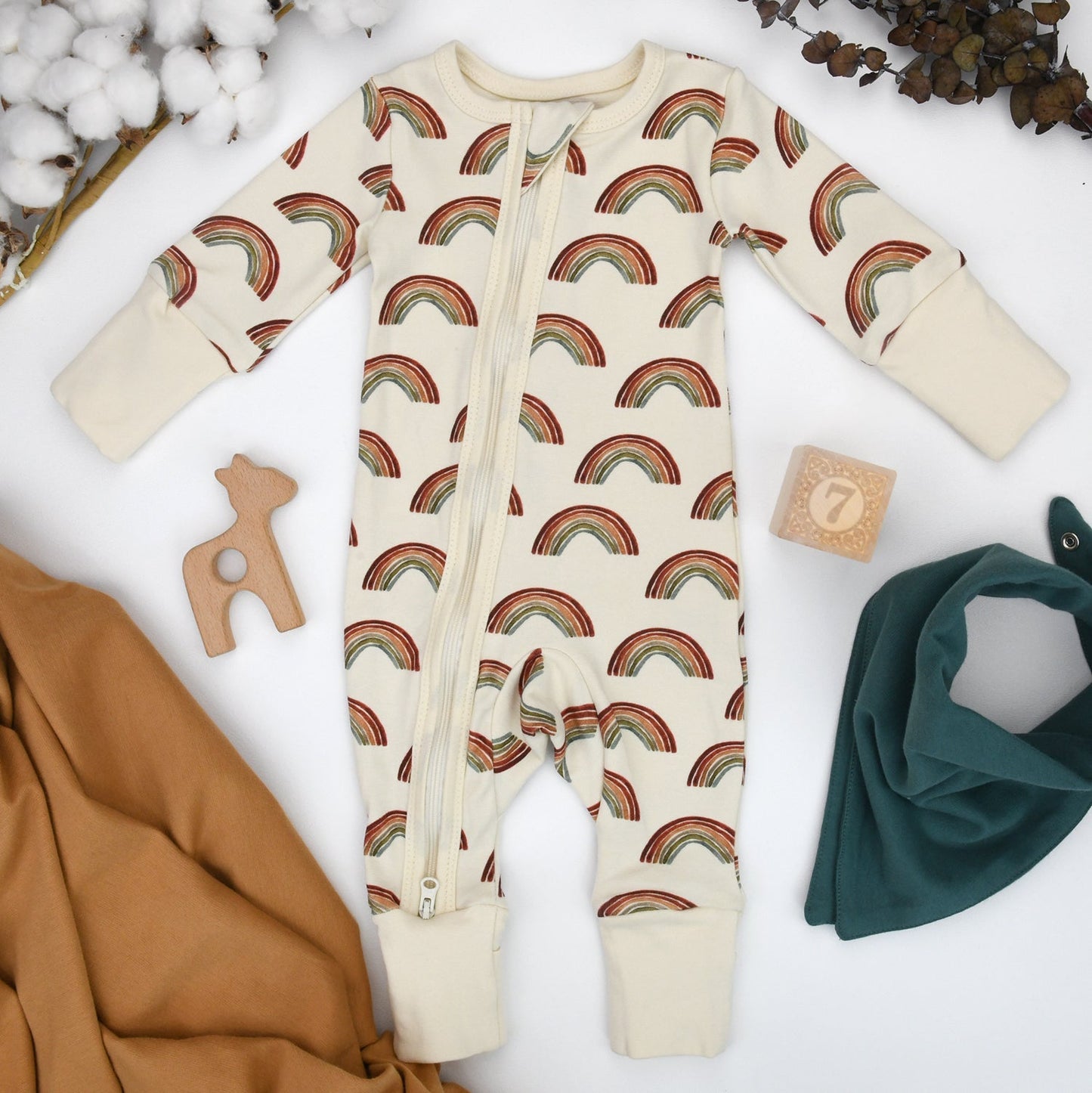 Baby onesie with rainbow pattern on a white background with accessories.