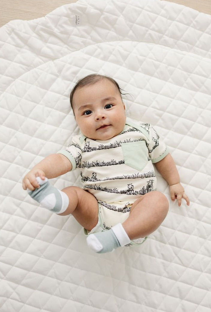 Baby lying on a quilted surface wearing a patterned onesie and socks.