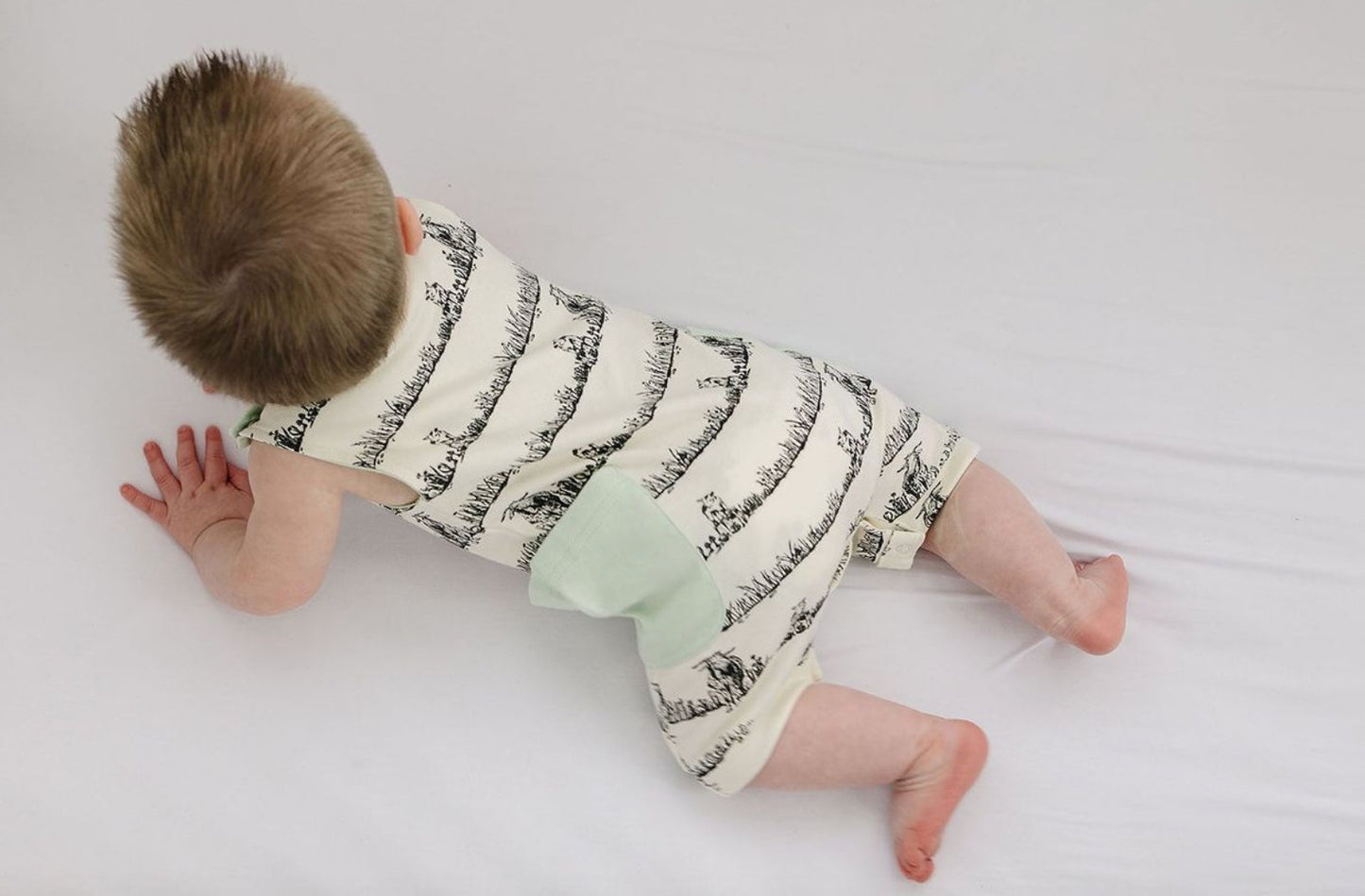 Baby crawling on a white surface wearing a patterned outfit with green accents.