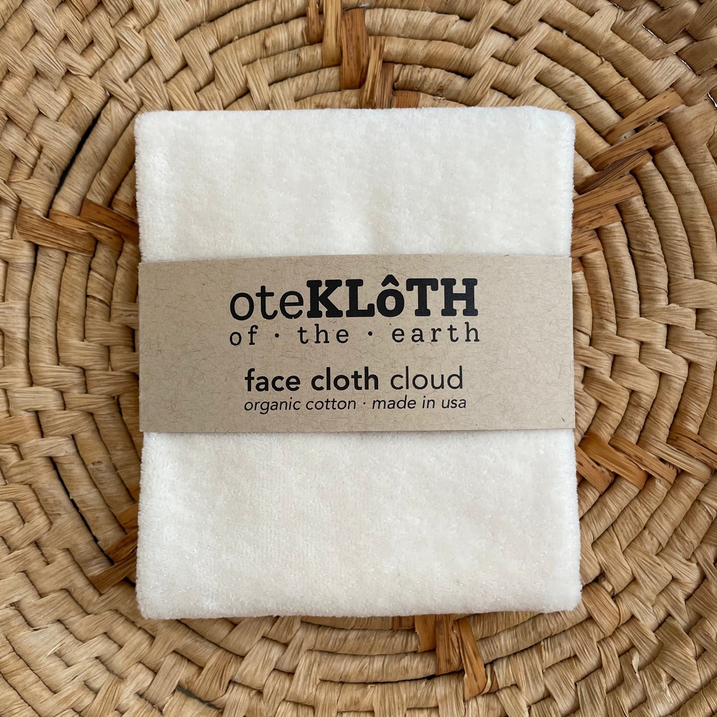Folded white face cloth with a brown label on a woven surface