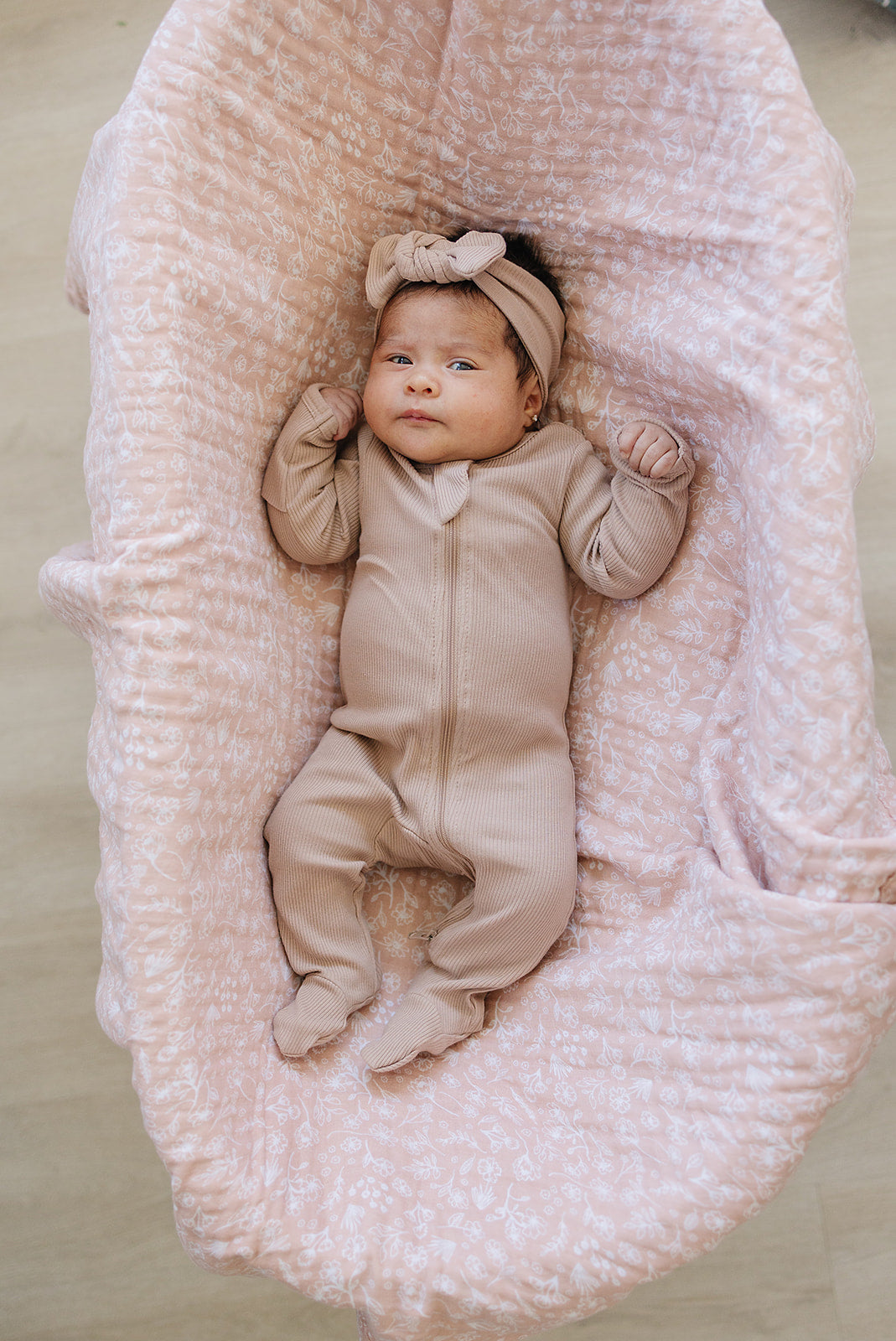 Newborn baby in a beige outfit lying on a textured pink blanket.