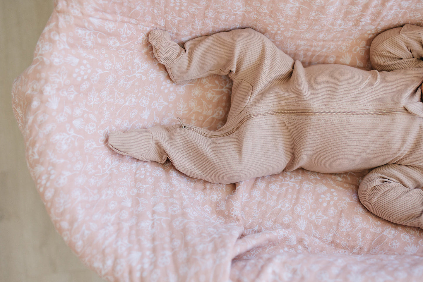 Baby in a beige onesie lying on a pink polka dot blanket