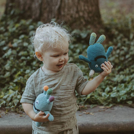 Child holding two blue stuffed monster toys in front of a tree